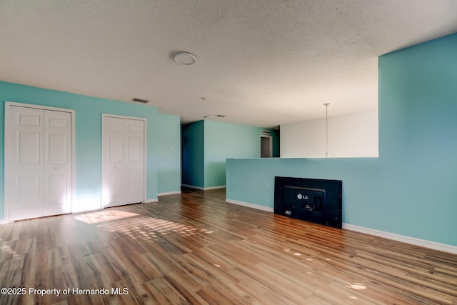 unfurnished living room with baseboards, visible vents, wood finished floors, and a textured ceiling