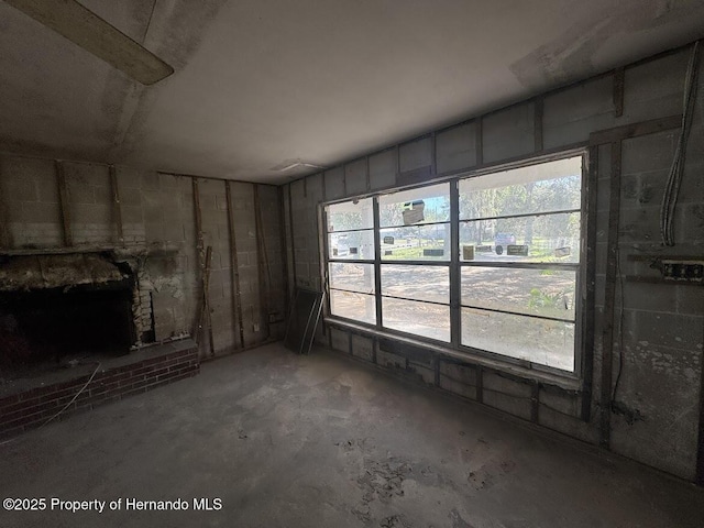 unfurnished living room featuring unfinished concrete floors, a fireplace with raised hearth, and a healthy amount of sunlight