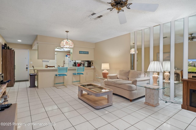 living room featuring a fireplace, a textured ceiling, a ceiling fan, light tile patterned floors, and visible vents