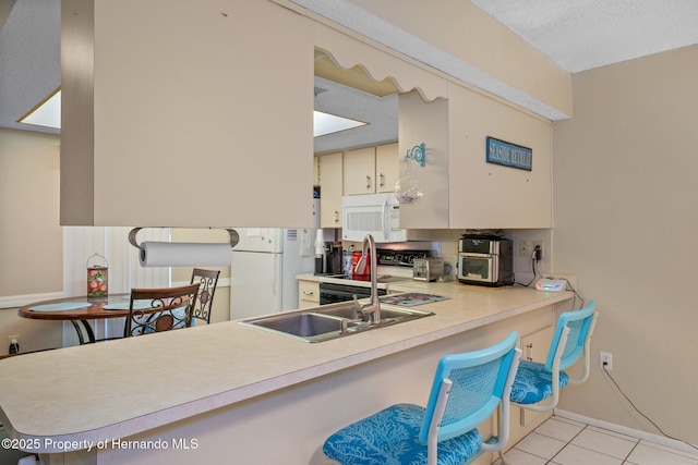 kitchen with a sink, light countertops, light tile patterned floors, black / electric stove, and white microwave