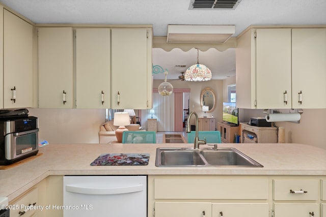 kitchen featuring visible vents, white dishwasher, light countertops, a sink, and cream cabinetry
