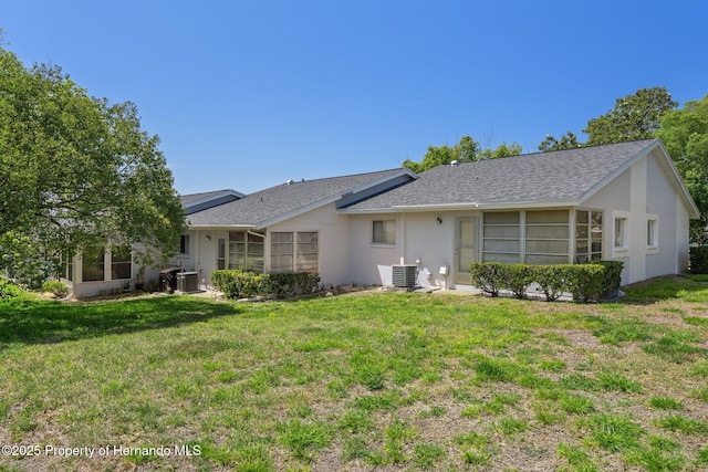 back of property with stucco siding, a yard, and central AC