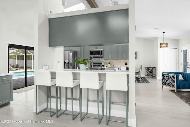 1156 Battersea Ave, Spring Hill, FL 34609 - kitchen featuring gray cabinets, a breakfast bar area, appliances with stainless steel finishes, decorative backsplash, and a towering ceiling