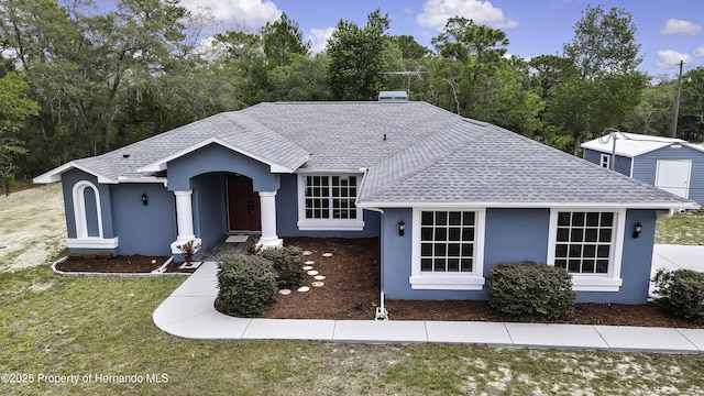 view of front of home with roof with shingles, stucco siding, and a front yard