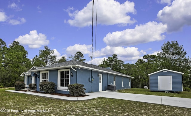 back of property with stucco siding, a storage unit, cooling unit, an outdoor structure, and a lawn