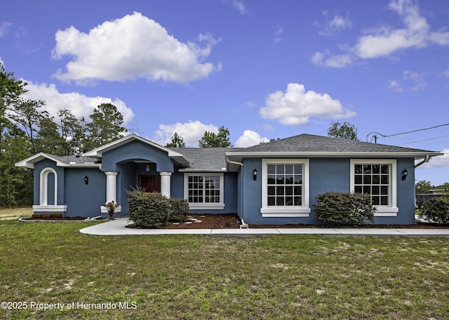 ranch-style home with stucco siding, a front yard, and roof with shingles