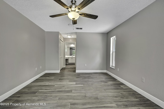 unfurnished bedroom featuring a textured ceiling, wood finished floors, baseboards, connected bathroom, and ceiling fan