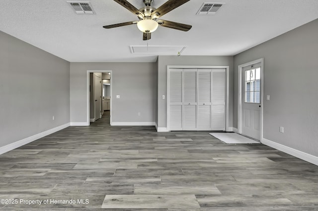 unfurnished bedroom with attic access, baseboards, wood finished floors, a closet, and ceiling fan