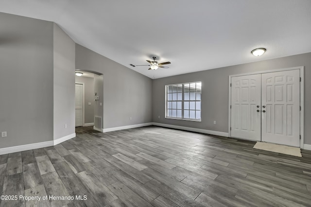 unfurnished living room featuring a ceiling fan, arched walkways, wood finished floors, vaulted ceiling, and baseboards