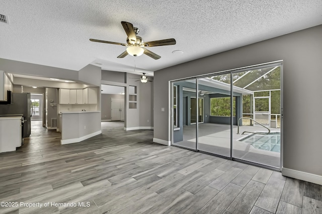 unfurnished living room featuring a ceiling fan, a textured ceiling, wood finished floors, baseboards, and healthy amount of natural light