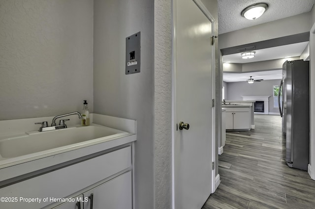 bathroom with vanity, ceiling fan, a textured ceiling, a textured wall, and wood finished floors