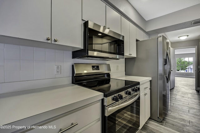 kitchen with stainless steel appliances, light countertops, decorative backsplash, light wood finished floors, and white cabinetry