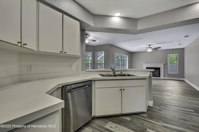 kitchen featuring dishwasher, a sink, ceiling fan, a glass covered fireplace, and a peninsula