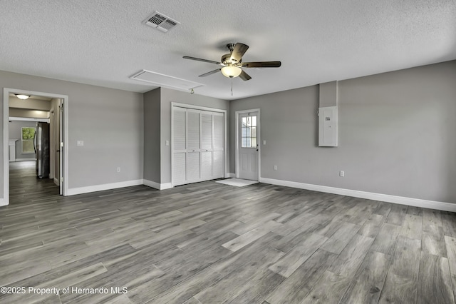unfurnished bedroom with attic access, a textured ceiling, baseboards, wood finished floors, and electric panel