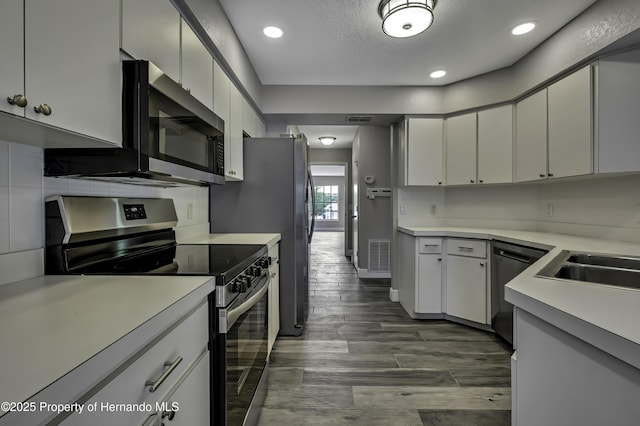 kitchen with stainless steel appliances, a sink, light countertops, dark wood finished floors, and recessed lighting