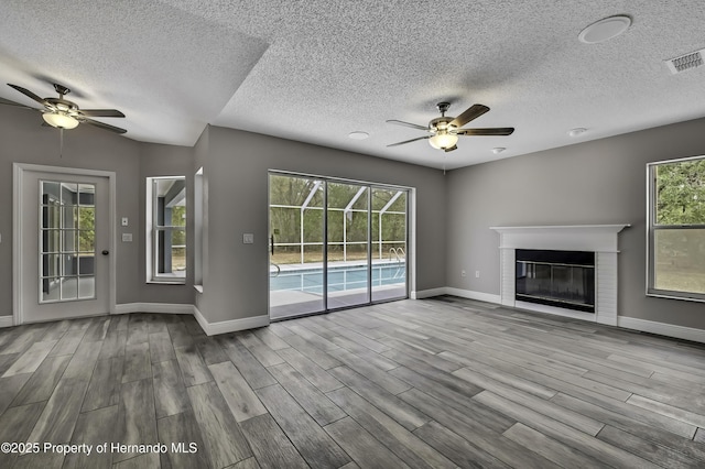 unfurnished living room featuring a ceiling fan, wood finished floors, baseboards, a glass covered fireplace, and a textured ceiling