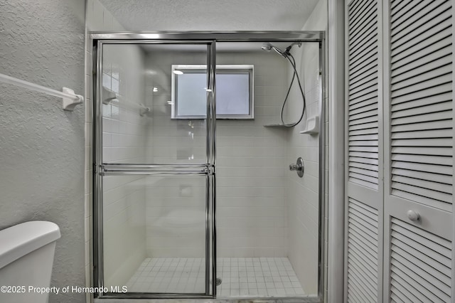 bathroom with a textured wall, a closet, toilet, and a stall shower