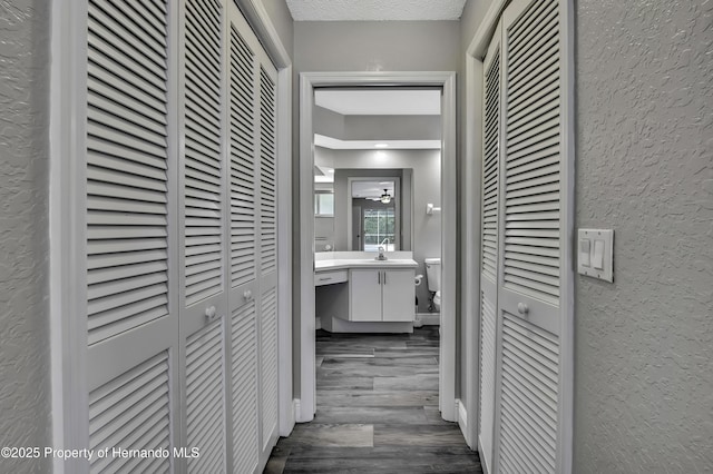 hall featuring a textured wall, a sink, dark wood finished floors, and a textured ceiling