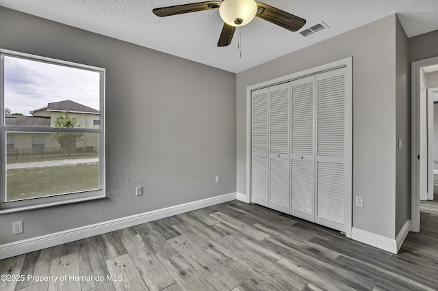 unfurnished bedroom featuring wood finished floors, baseboards, a closet, a textured ceiling, and ceiling fan