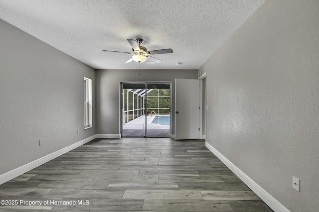 empty room featuring a ceiling fan, a textured ceiling, wood finished floors, baseboards, and a textured wall