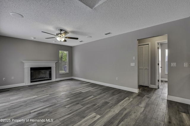 unfurnished living room featuring a ceiling fan, a textured ceiling, dark wood finished floors, a fireplace with flush hearth, and baseboards