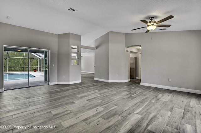unfurnished living room featuring ceiling fan, arched walkways, wood finished floors, baseboards, and vaulted ceiling