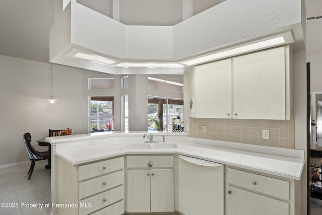 kitchen featuring light countertops, a sink, tasteful backsplash, dishwasher, and a peninsula