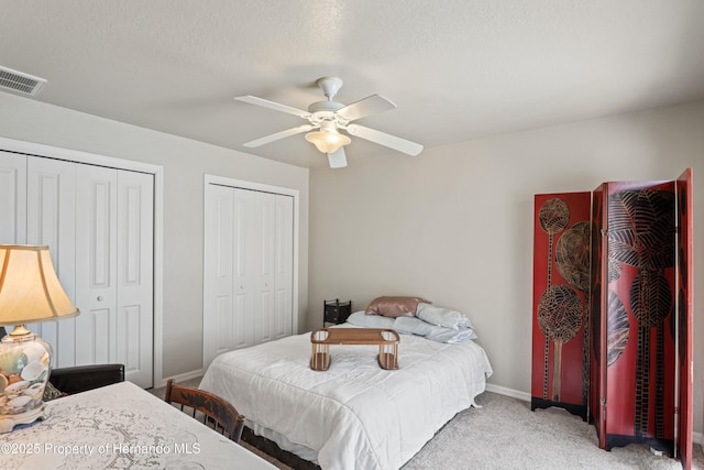 bedroom with a ceiling fan, multiple closets, baseboards, light colored carpet, and visible vents