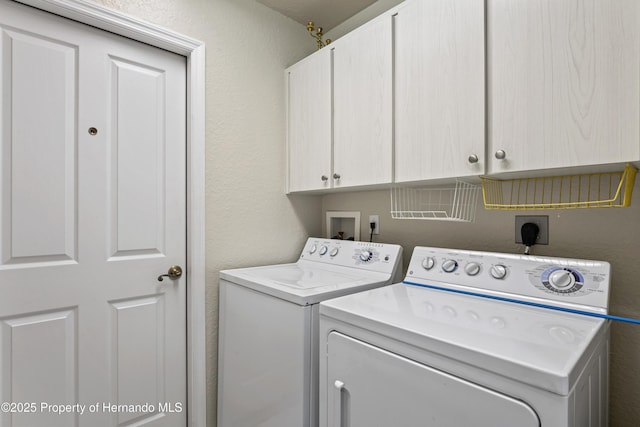 laundry room with a textured wall, cabinet space, and washer and clothes dryer