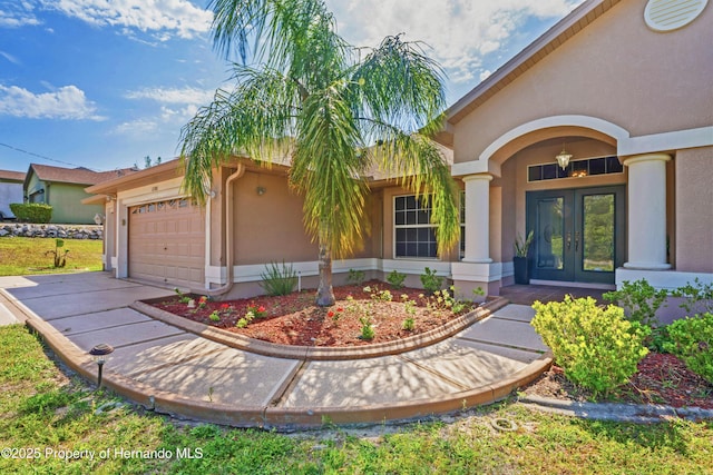 entrance to property with stucco siding, an attached garage, french doors, and concrete driveway