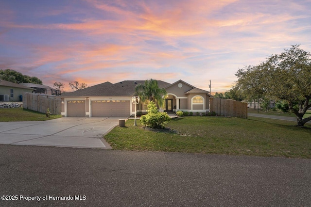 view of front facade with driveway, stucco siding, fence, a front lawn, and a garage