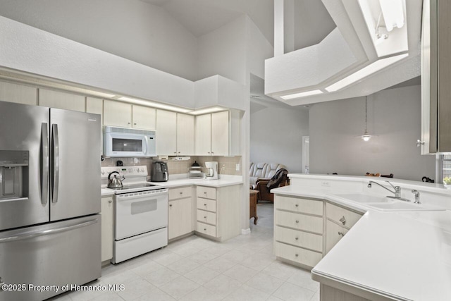 kitchen featuring light tile patterned flooring, light countertops, a peninsula, white appliances, and a sink