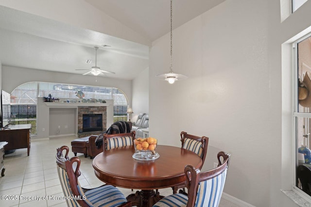 dining space with a fireplace, lofted ceiling, light tile patterned floors, baseboards, and ceiling fan