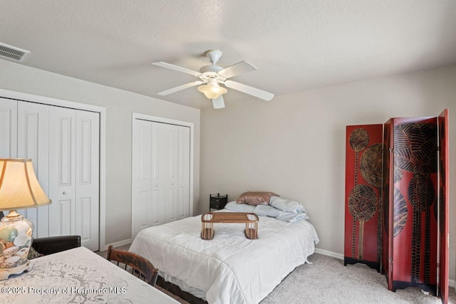 bedroom with multiple closets, visible vents, baseboards, a ceiling fan, and light carpet