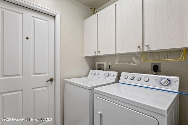 laundry room with a textured wall, cabinet space, and washer and clothes dryer