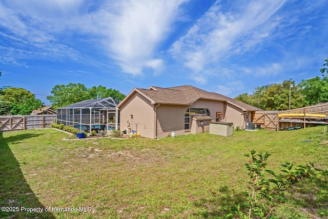 rear view of house with glass enclosure, a fenced backyard, stucco siding, and a yard
