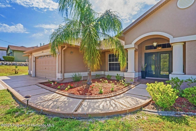 property entrance featuring stucco siding, an attached garage, french doors, and concrete driveway