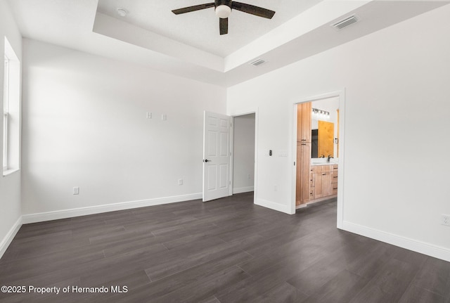 16043 Penn State Rd, Weeki Wachee, FL 34614 - unfurnished bedroom with a tray ceiling, dark wood finished floors, baseboards, and ensuite bath