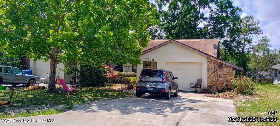 7372 Canterbury St, Spring Hill, FL 34606 - obstructed view of property featuring driveway, stone siding, an attached garage, and stucco siding