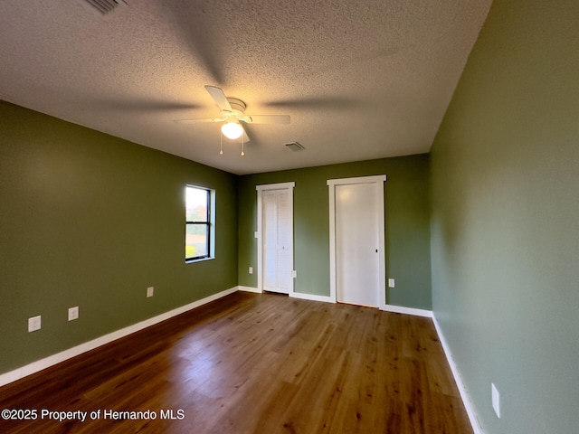 2253 Estill Ave, Spring Hill, FL 34609 - unfurnished bedroom featuring two closets, dark wood-type flooring, baseboards, a textured ceiling, and a ceiling fan