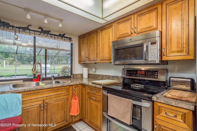 18216 Monteverde Dr, Shady Hills, FL 34610 - kitchen featuring light tile patterned floors, a sink, appliances with stainless steel finishes, and brown cabinetry