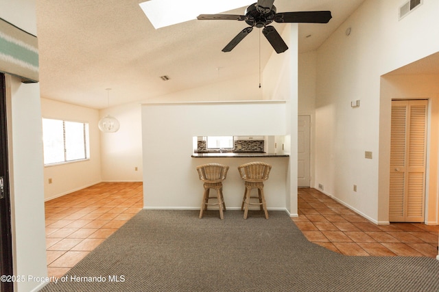 interior space featuring a kitchen bar, a ceiling fan, visible vents, carpet floors, and tile patterned floors