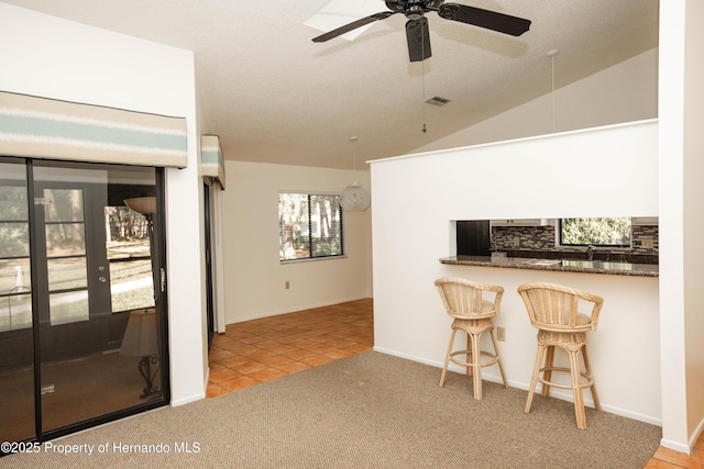 interior space with vaulted ceiling, tile patterned floors, visible vents, ceiling fan, and carpet