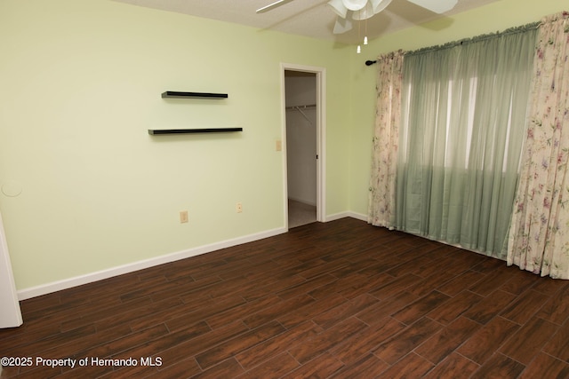 unfurnished bedroom with a closet, baseboards, a spacious closet, a ceiling fan, and dark wood-style floors