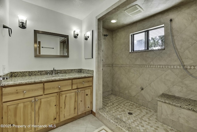 full bath featuring tiled shower, vanity, and tile patterned flooring