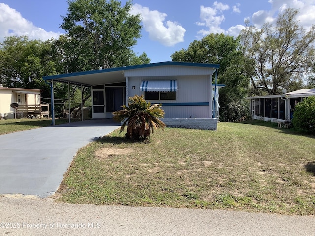 manufactured / mobile home with a front yard, an attached carport, a sunroom, and concrete driveway