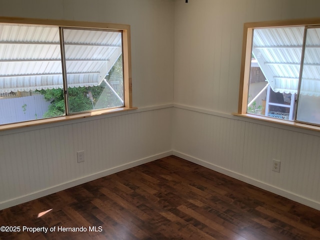 spare room featuring wainscoting, baseboards, and dark wood-style floors
