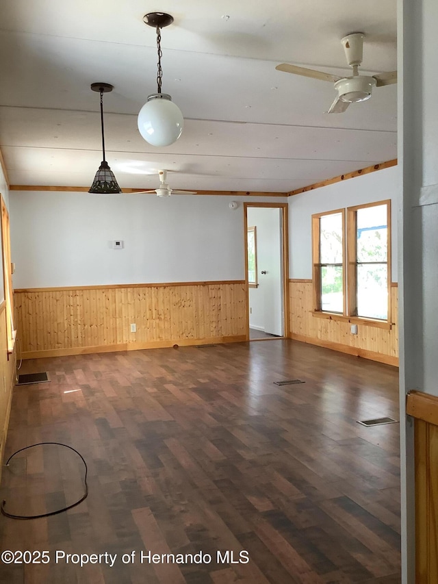 unfurnished room with visible vents, a ceiling fan, wooden walls, dark wood-type flooring, and a wainscoted wall