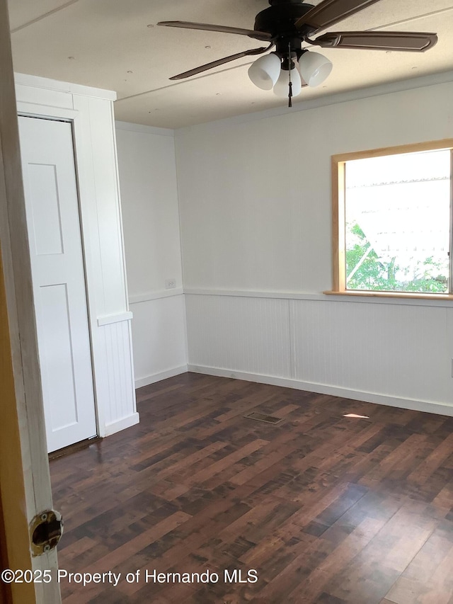 spare room featuring dark wood-style floors, a ceiling fan, and a wainscoted wall