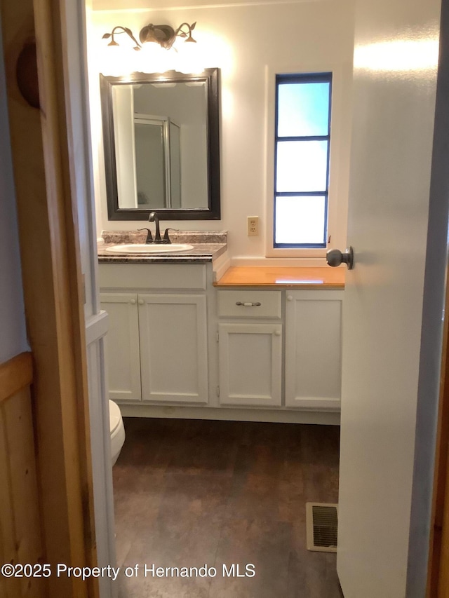 bathroom featuring toilet, vanity, and visible vents